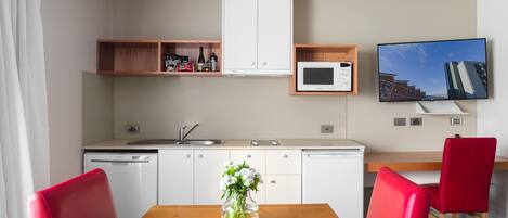 A modern kitchen with white cabinets, a microwave, and a dining area with a wooden table and red chairs.