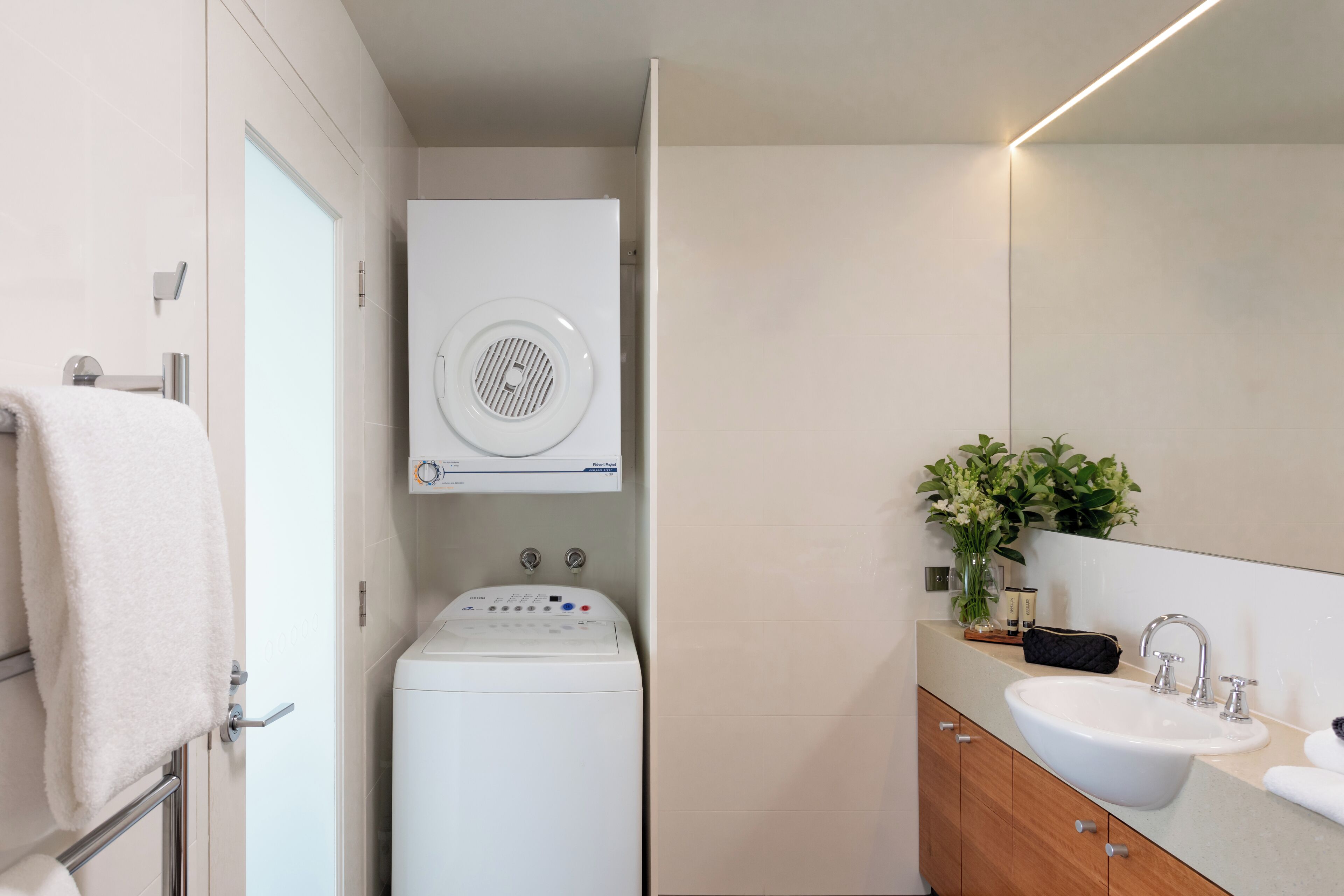 Uma casa de banho moderna com máquina de lavar e secar integradas, uma pia e um espelho.