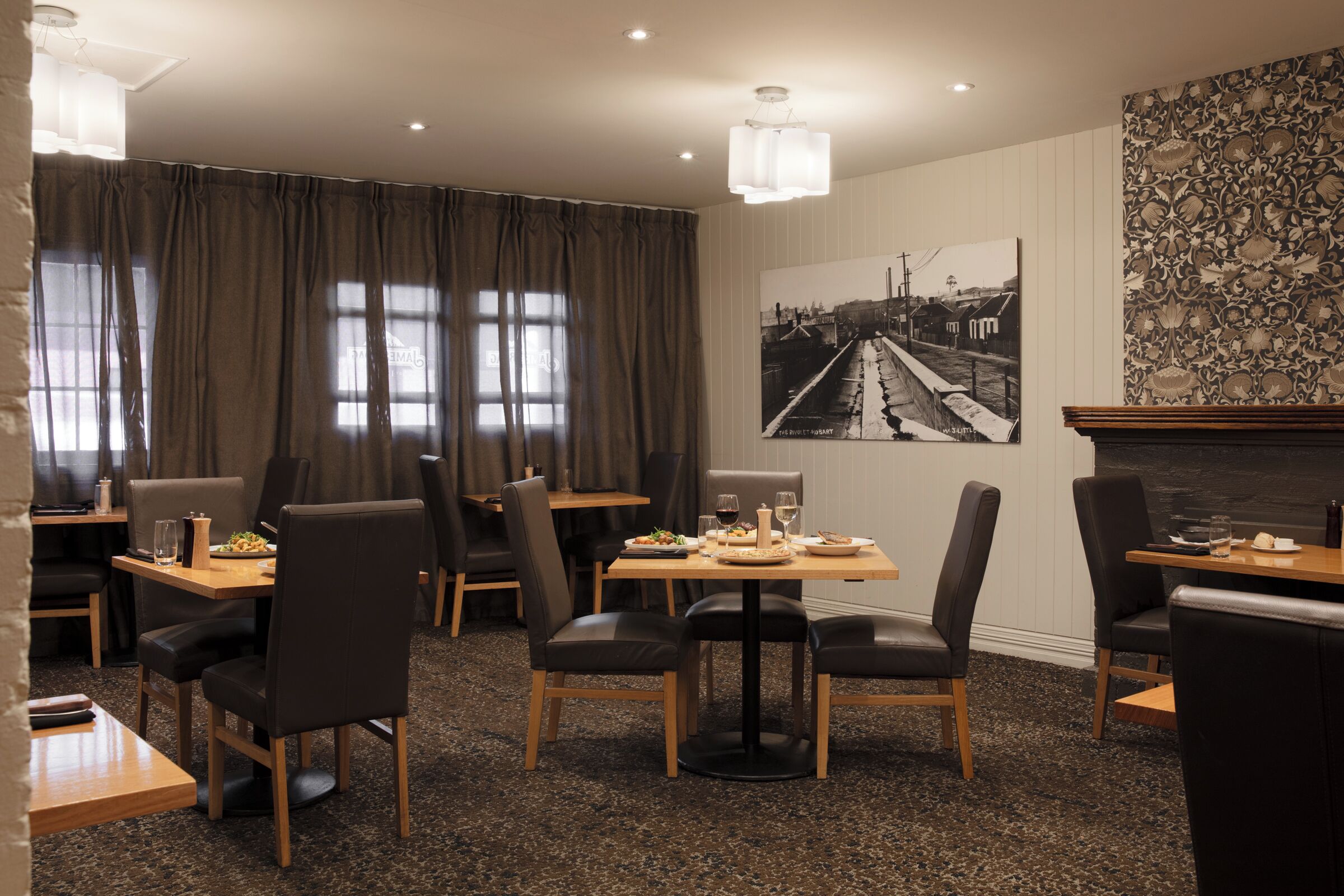 A dining area with tables and chairs, a large window with curtains, and a wall-mounted picture.