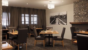 A dining area with tables and chairs, a large window with curtains, and a wall-mounted picture.