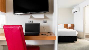 A hotel room with a bed, a desk with a laptop, a TV, and an air conditioning unit.
