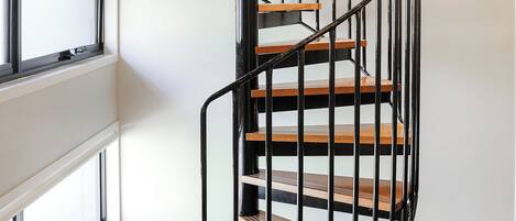 A spiral staircase with wooden steps and black metal railings in a room with large windows and carpeted flooring.