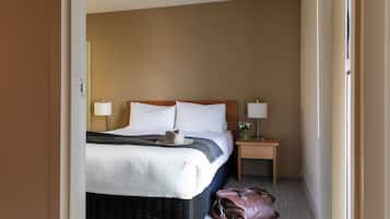 Una habitación de hotel con cama, lámparas de noche, una mesita de noche y un bolso en el suelo.