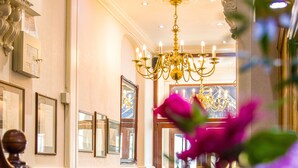 A hotel lobby with a chandelier, framed pictures, and a blue chair. - London Town Hotel (London)