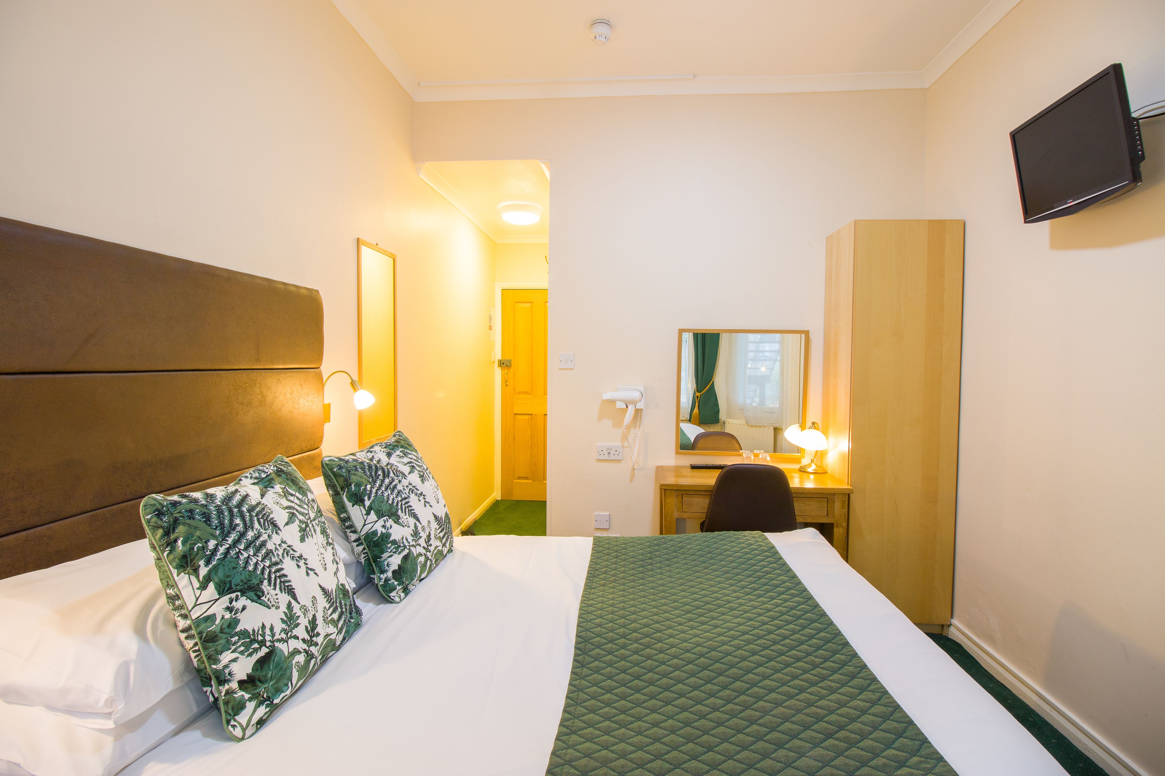 A hotel room with a bed, a desk, a chair, a mirror, and a television on the wall.