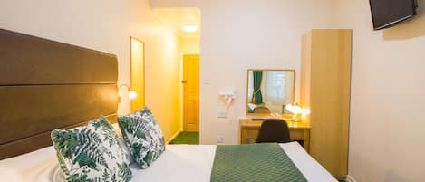 A hotel room with a bed, a desk, a chair, a mirror, and a television on the wall.