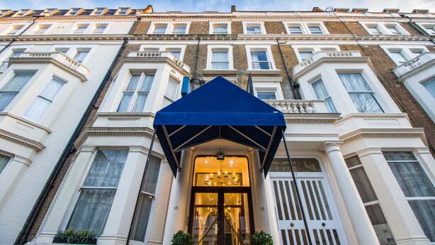 A multi-story building with a prominent entrance featuring a blue awning and a large glass door. - London Town Hotel (London)