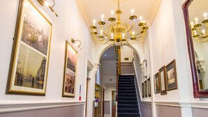 A grand hallway with a chandelier, framed pictures, and a staircase. - London Town Hotel (London)