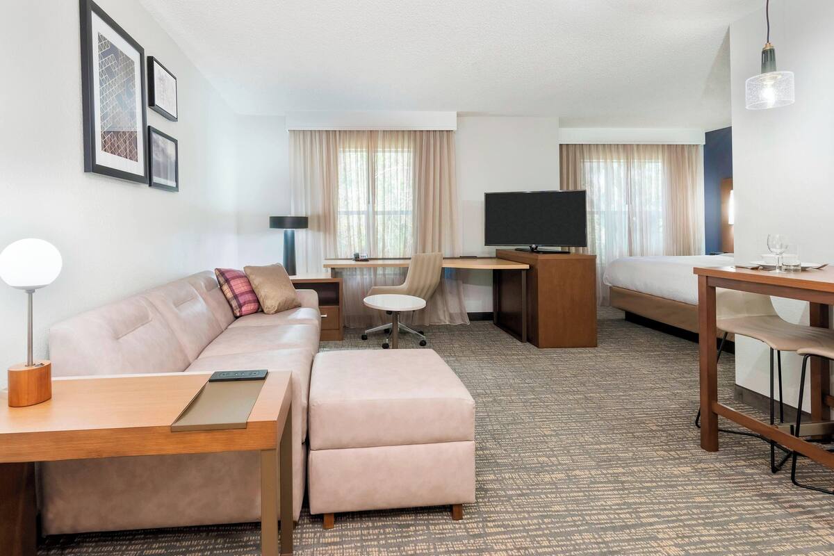 Ein Hotelzimmer mit einer Couch, einem Schreibtisch, einem Fernseher, einem Bett und einem kleinen Tisch.