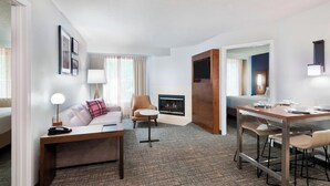 Een hotelkamer met een bank, fauteuil, klein tafeltje en een eethoek met een tafel en stoelen.