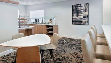 A conference room with a white table, beige chairs, a buffet counter with food display, and a patterned carpet.