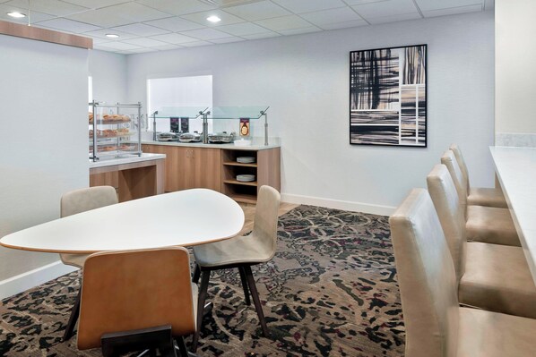 Un salón de conferencias con una mesa blanca, sillas color beige, un mostrador de buffet con comida y una alfombra estampada.
