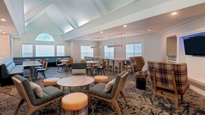 Een ruime hotel lobby met een hoge plafond, grote ramen en diverse zithoekjes, waaronder banken, stoelen en poefs.