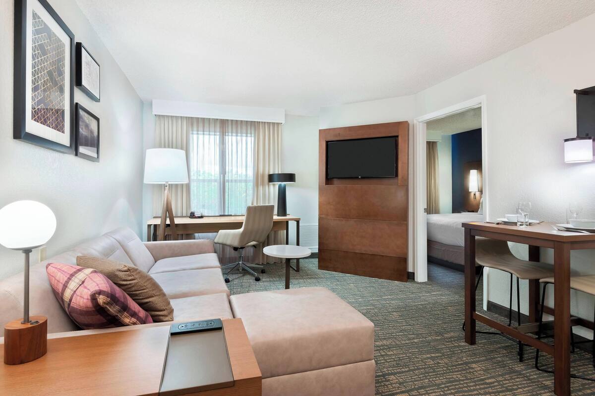 Ein Hotelzimmer mit einer Couch, einem Schreibtisch, einem Esstisch, einem Fernseher und einem Bett.