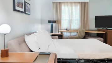 A hotel room with a bed, a desk, a chair, a TV, and a lamp.