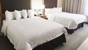 A hotel room with two beds, each with white linens and a headboard. There is a bedside table with a lamp and a phone. The room has a neutral color scheme with beige walls and curtains. - Hampton Inn & Suites Cleveland/Independence (Independence)