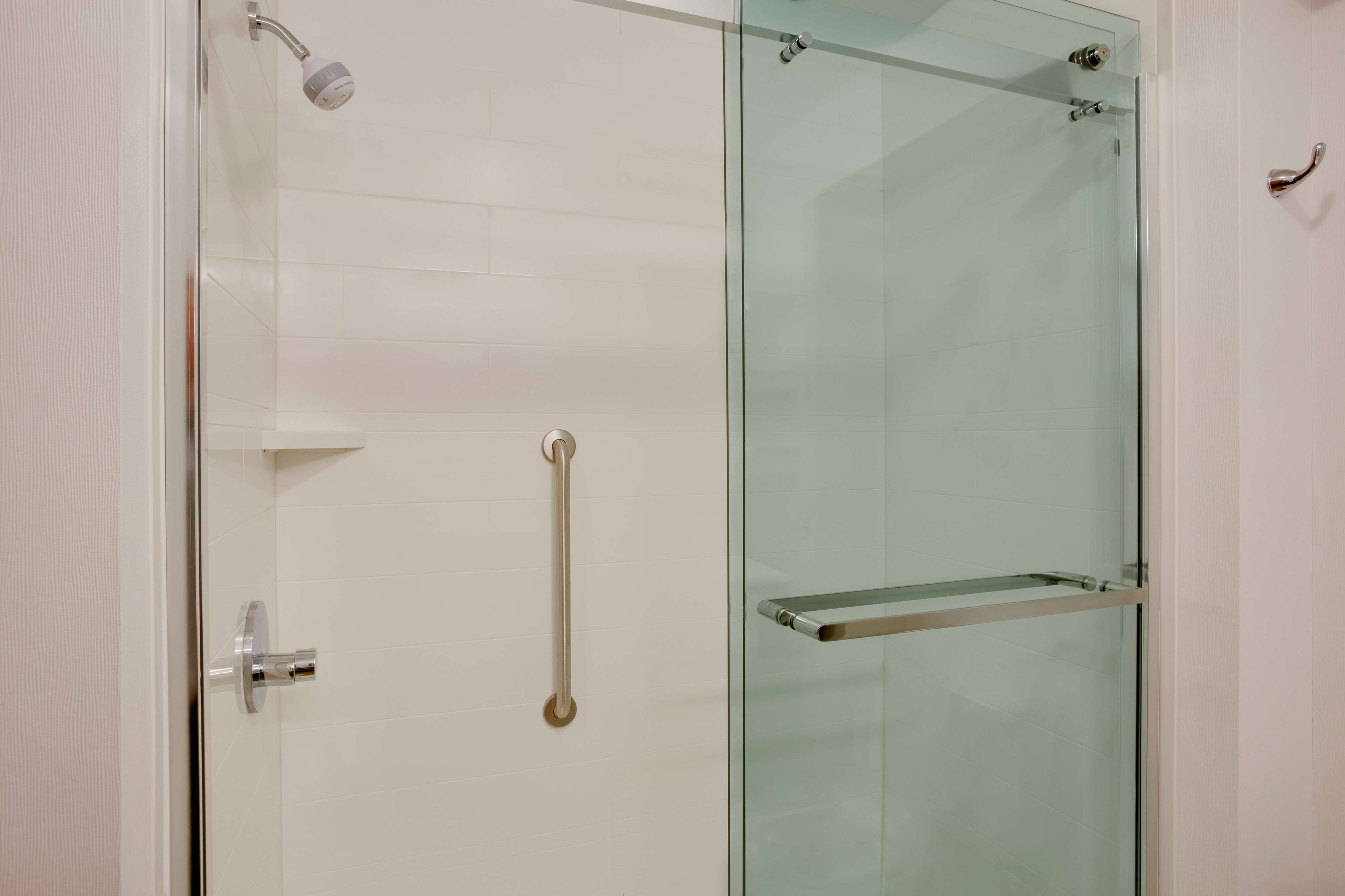 A modern bathroom with a glass shower enclosure, a white tiled wall, and a metal grab bar.