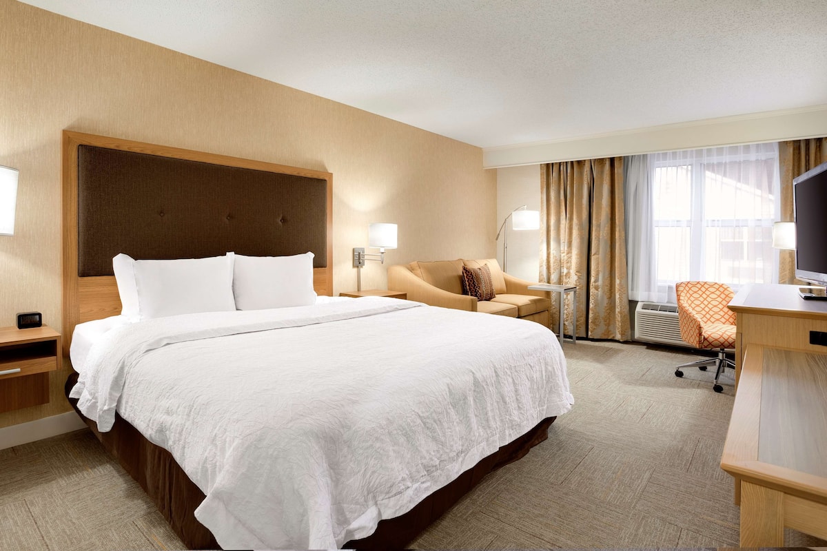 A hotel room with a large bed, a desk with a chair, a sofa, and a TV.