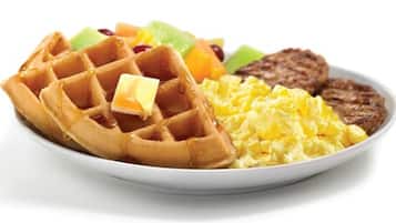 Um prato com waffles, ovos mexidos e um pedaço de carne.