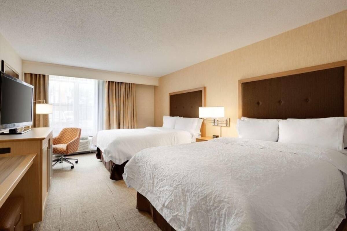 A hotel room with two beds, a desk, a TV, and a chair.