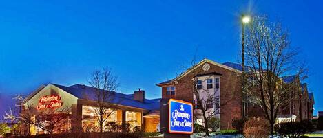Ein Hampton Inn Suites Hotel mit gut beleuchteter Fassade und verschneiter Landschaft.