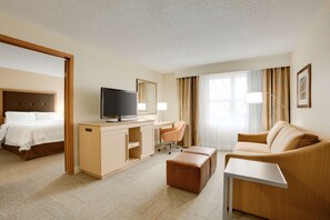A hotel room with a bed, a desk with a TV, a chair, a sofa, and a small table.