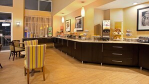 A modern kitchen with a long counter, various food stations, and a dining area with chairs. - Hampton Inn & Suites Cleveland/Independence (Independence)