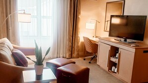 A modern hotel room with a sofa, ottoman, desk, and television. - Hampton Inn & Suites Cleveland/Independence (Independence)