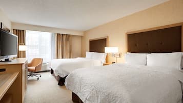A hotel room with two beds, a desk, a TV, and a chair.
