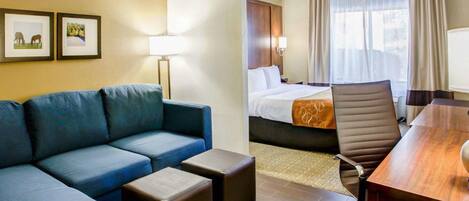 A hotel room with a sofa, two ottomans, a desk, and a chair.