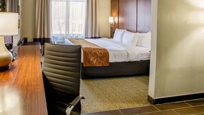 A hotel room with a bed, a desk with a lamp, a chair, and a large window with curtains. - Comfort Suites Georgetown (Georgetown)