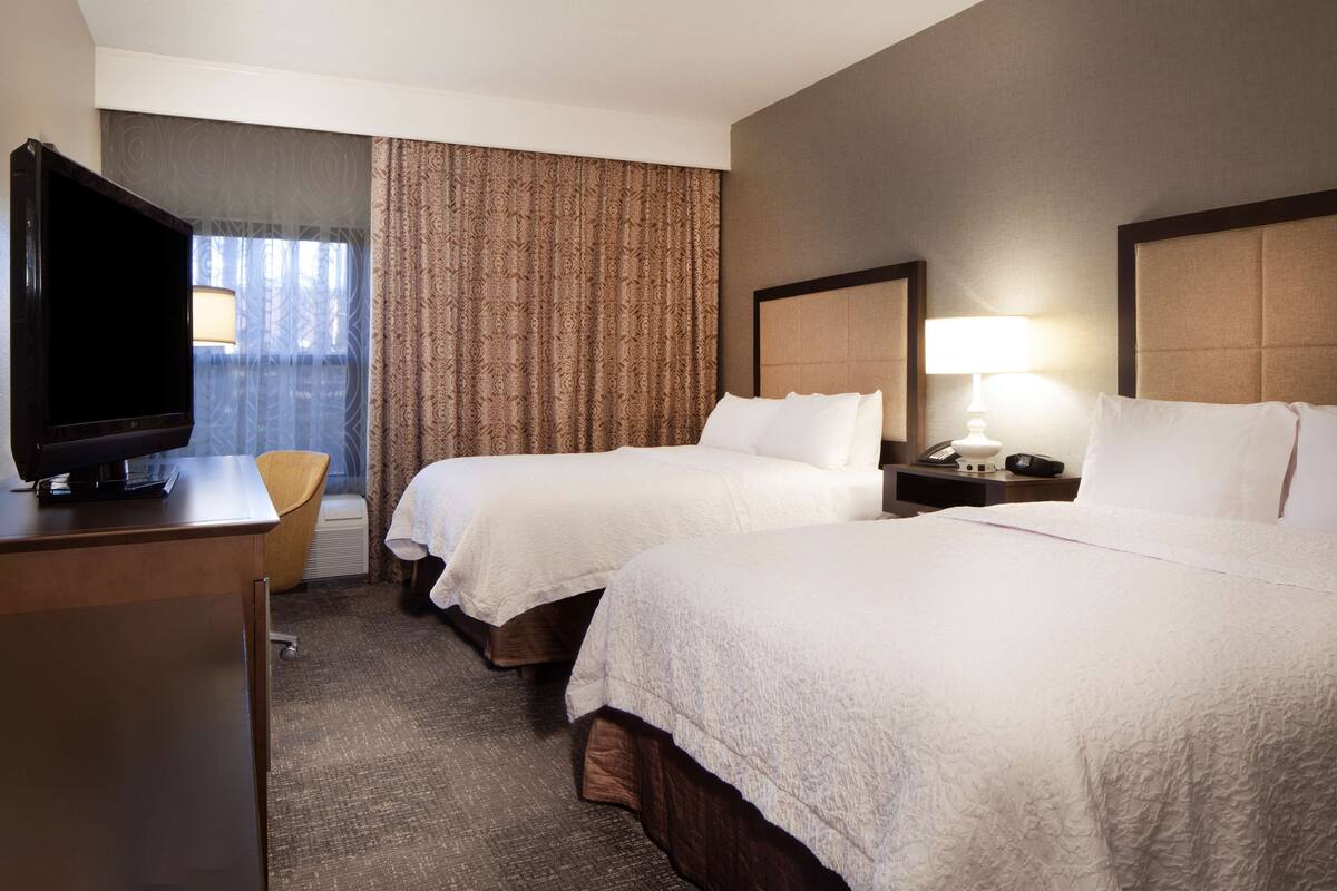 A hotel room with two beds, a TV, a desk, and a chair.