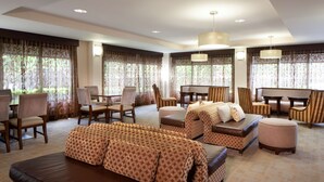 A spacious hotel lobby with a large seating area, including sofas and chairs, a piano, and a dining table.