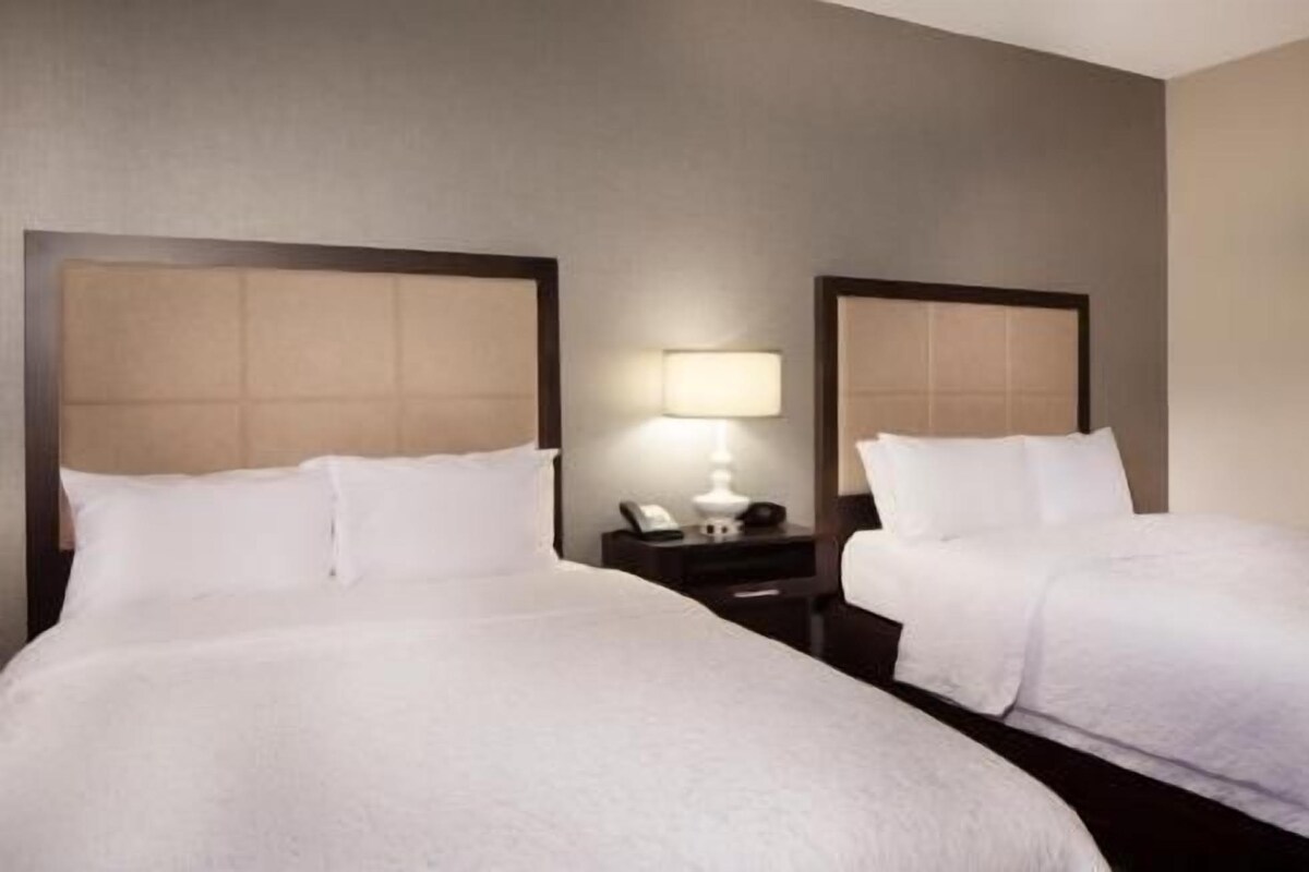 Habitación de hotel con dos camas, una mesita de noche con lámpara y un teléfono instalado en la pared.