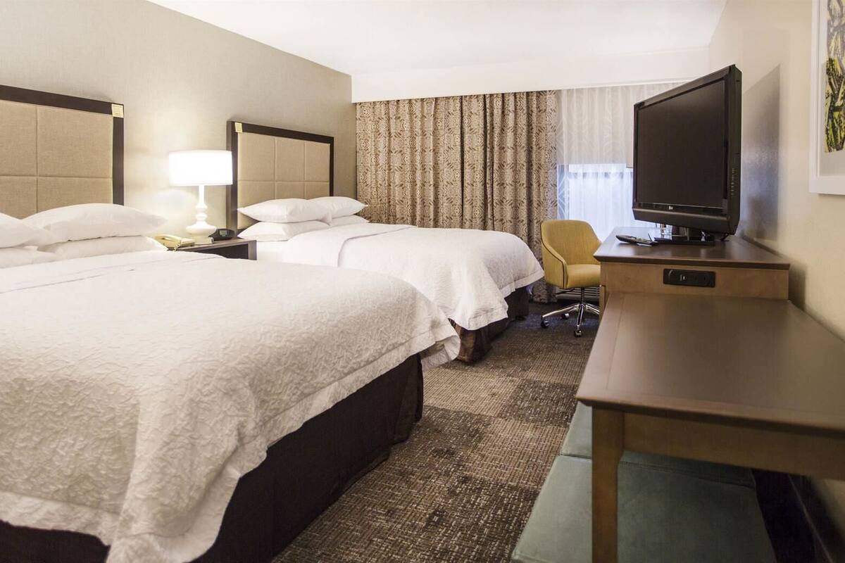 A hotel room with two beds, a desk, a chair, a television, and a window with curtains.