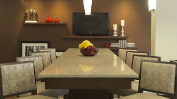 A conference room with a long table, patterned chairs, a television, and a fruit bowl.