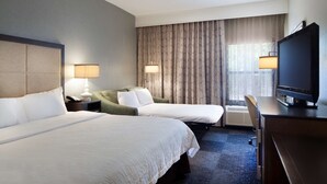 A hotel room with two beds, a desk, a television, and a window with curtains.