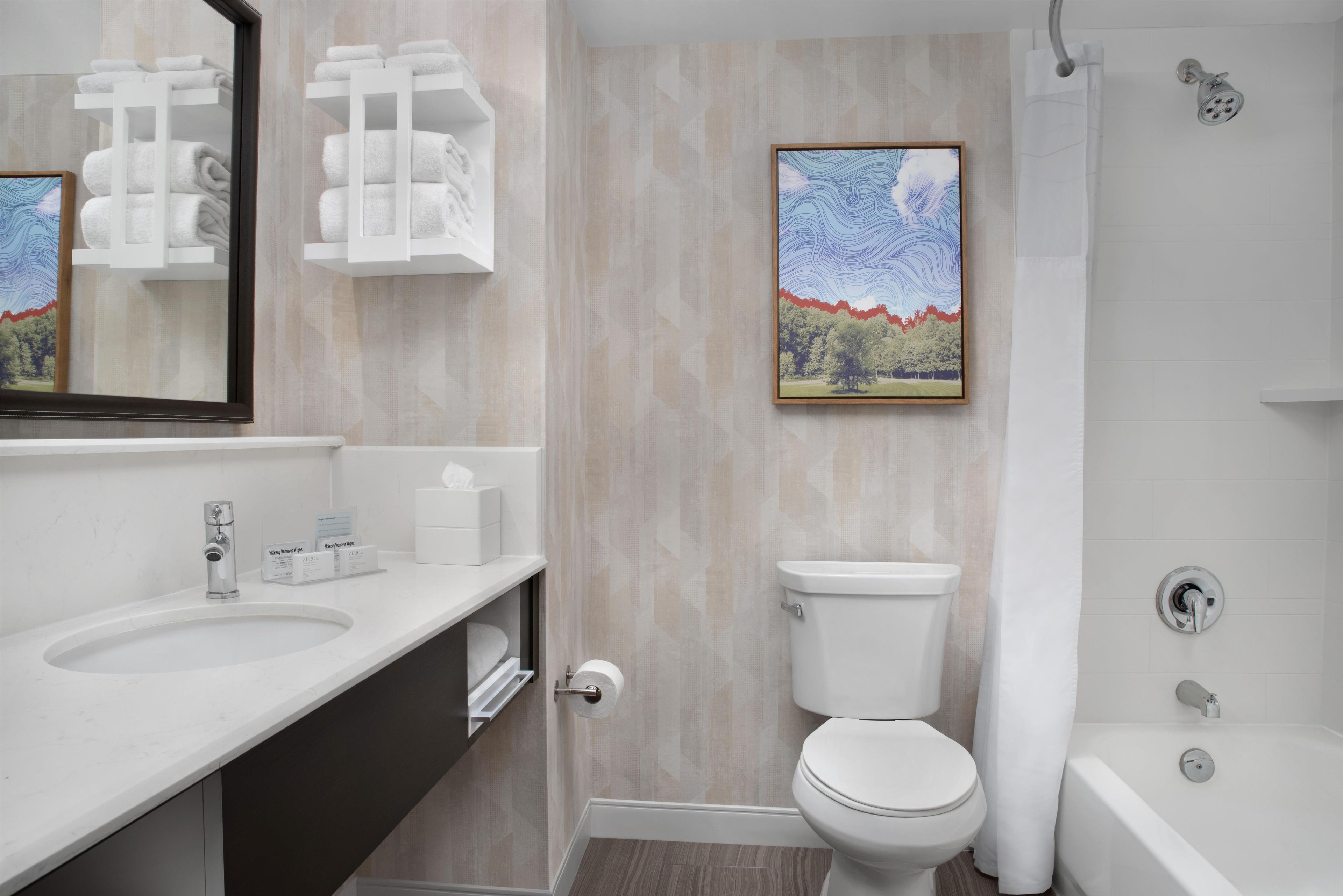 A modern bathroom with a toilet, sink, and shower. There is a framed picture on the wall.