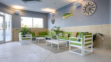 A modern lounge area with green and white furniture, a large wall clock, and a view through the glass doors.