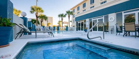 A pool area with lounge chairs and a building with large windows.