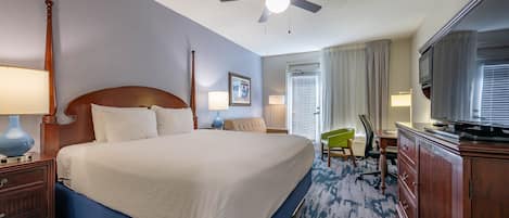 A hotel room with a large bed, a ceiling fan, a TV, and a desk with a chair.