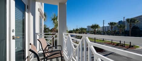 A balcony with two chairs and a white railing overlooking a street with palm trees and buildings.