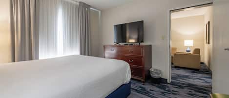A hotel room with a bed, a television on a dresser, a ceiling fan, and a view into the hallway.