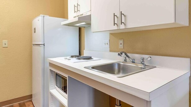 Una cocina compacta con armarios blancos, un lavamanos de acero inoxidable y un horno empotrado.