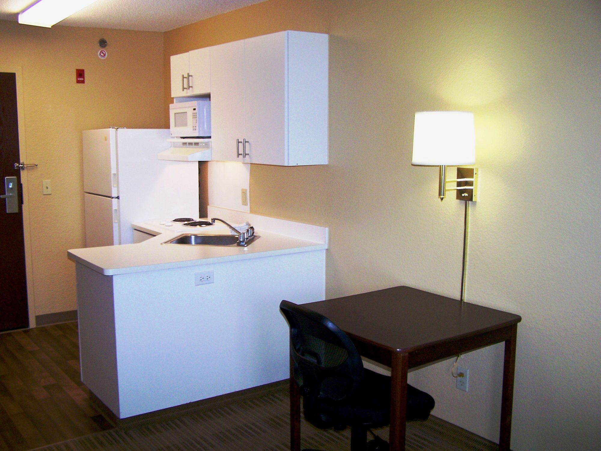 Una kitchenette compacta con refrigerador, microondas, pileta y una pequeña mesa con una silla.
