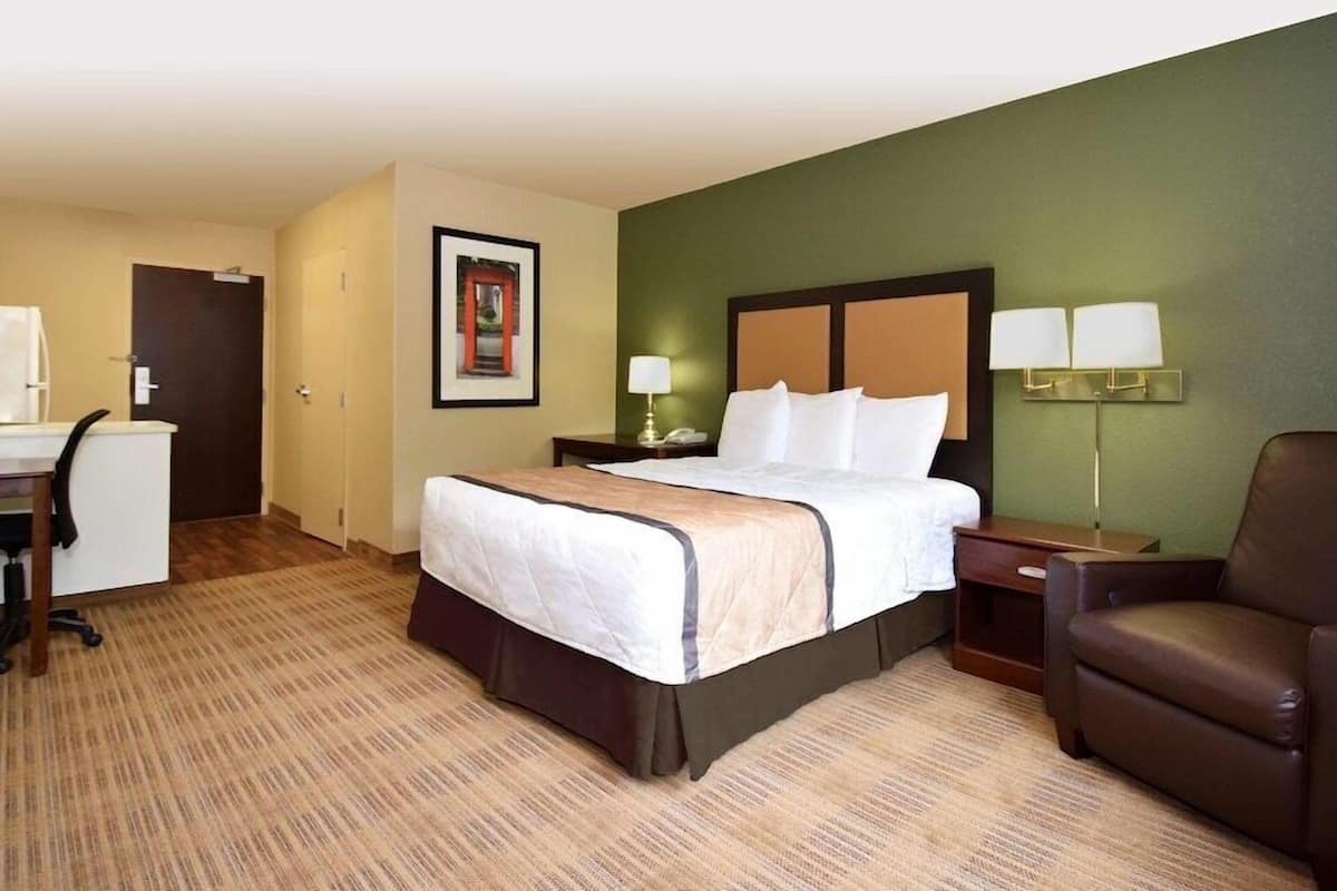 Una habitación de hotel con cama, escritorio, silla y mesita de noche.