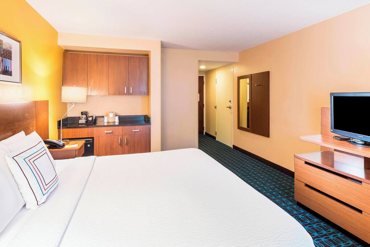 A hotel room with a large bed, a desk with a lamp, a television, and a bathroom door.