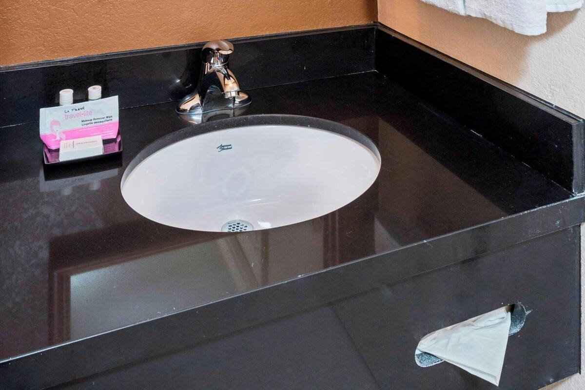 A bathroom with a black countertop, a white sink, a large mirror, and a towel rack with towels.