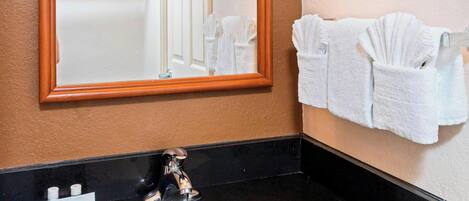 Un baño con encimera negra, lavabo blanco, un espejo grande y un perchero con toallas.