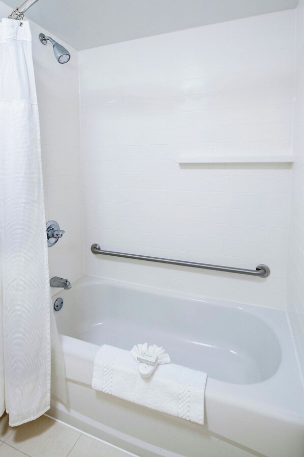 Una bañera blanca con una barra de apoyo, una toalla y un cortinón de ducha.